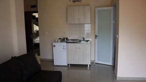 A compact living space with a kitchenette, a sofa, and a door leading to another room.