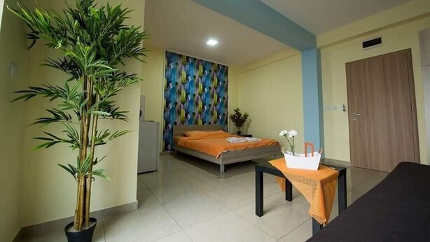 A hotel room with a bed, a small table with a vase, a potted plant, and a colorful wall.