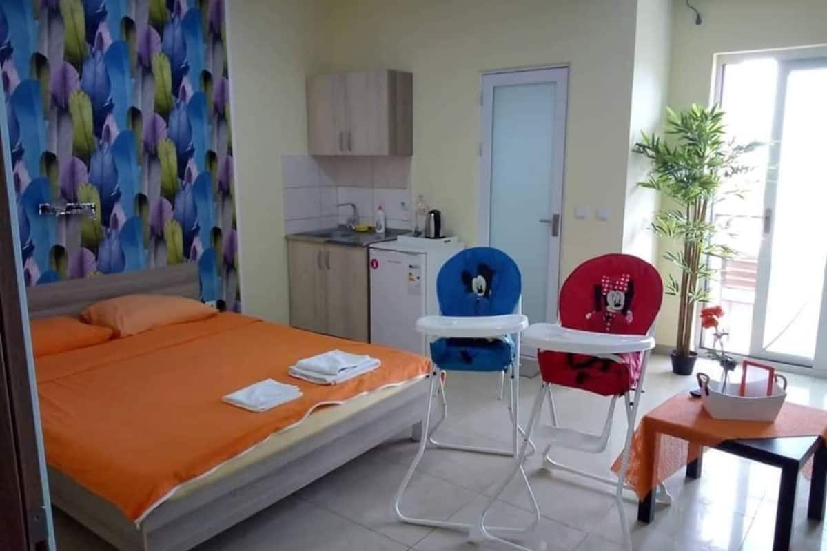 A hotel room with a bed, a desk, a chair, a small table, a potted plant, and a window.