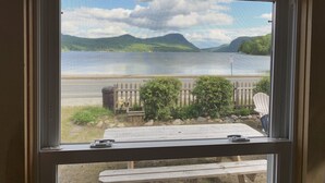 A window with a view of a backyard, including a wooden deck, a barbecue grill, and a fence. - Gebhardt Getaway - Charming LAKEFRONT Cottage on Lake Willoughby (Westmore)