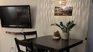 A dining area with a dark wooden table, black chairs, a hanging light fixture, and a mounted flat-screen TV.