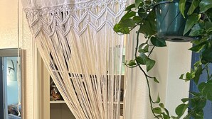 A bathroom with a macrame curtain, a sink, a mirror, and a potted plant.