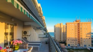 Un balcon avec une table dressée pour le dîner, offrant une vue sur un paysage urbain avec de hauts immeubles et un ciel dégagé.