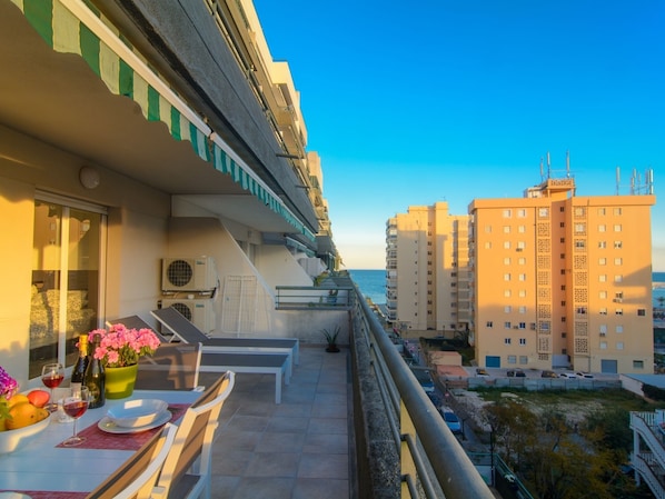 A balcony with a table set for dining, overlooking a cityscape with tall buildings and a clear sky.