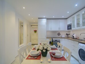 Una cocina moderna con armarios blancos, una mesa de comedor con platos, un florero y una copa de vino.