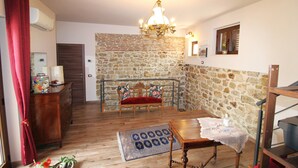 A cozy living room with a stone wall, a wooden dining table, a red sofa, and a chandelier.