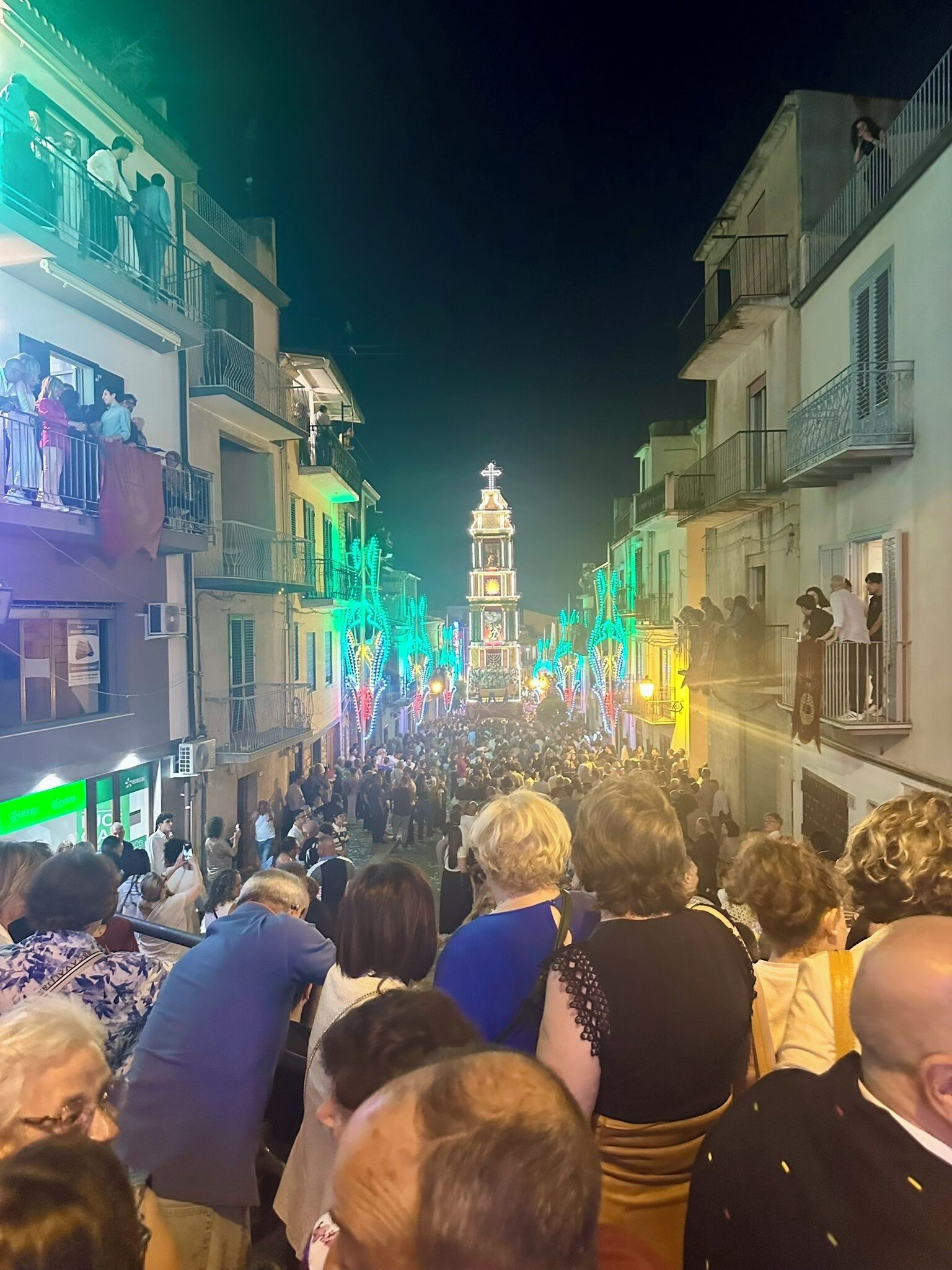Rua movimentada com pessoas reunidas em volta de uma torre iluminada.