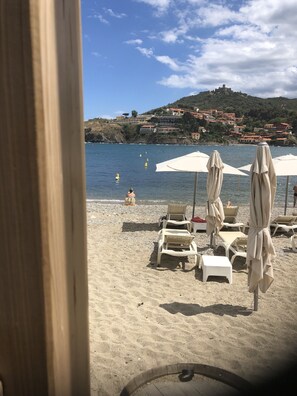 A beach with sun loungers and umbrellas, a clear sky, and buildings in the background. - Charming in Collioure – where creativity meets the beach (Collioure)
