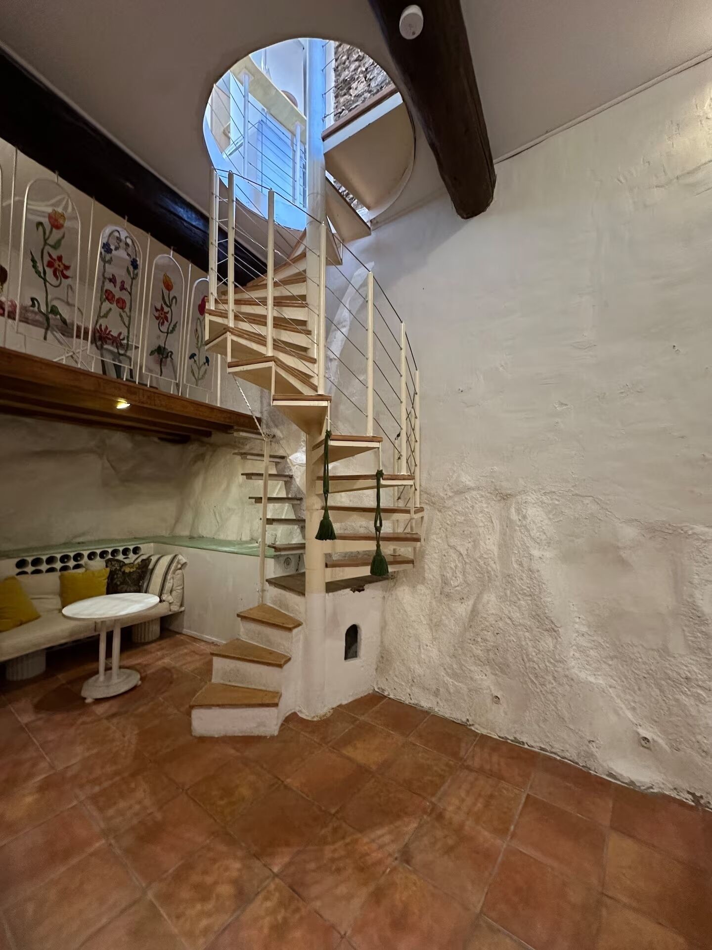 Una escalera de caracol en una habitación con pared blanca y tragaluz circular.