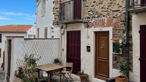 A stone building with a wooden table and chairs outside, a red door, and a balcony with a metal railing. - Charming in Collioure – where creativity meets the beach (Collioure)