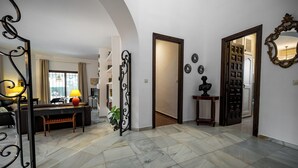 Un pasillo con suelo de mármol, un sofá, una mesa con una lámpara y un espejo decorativo.
