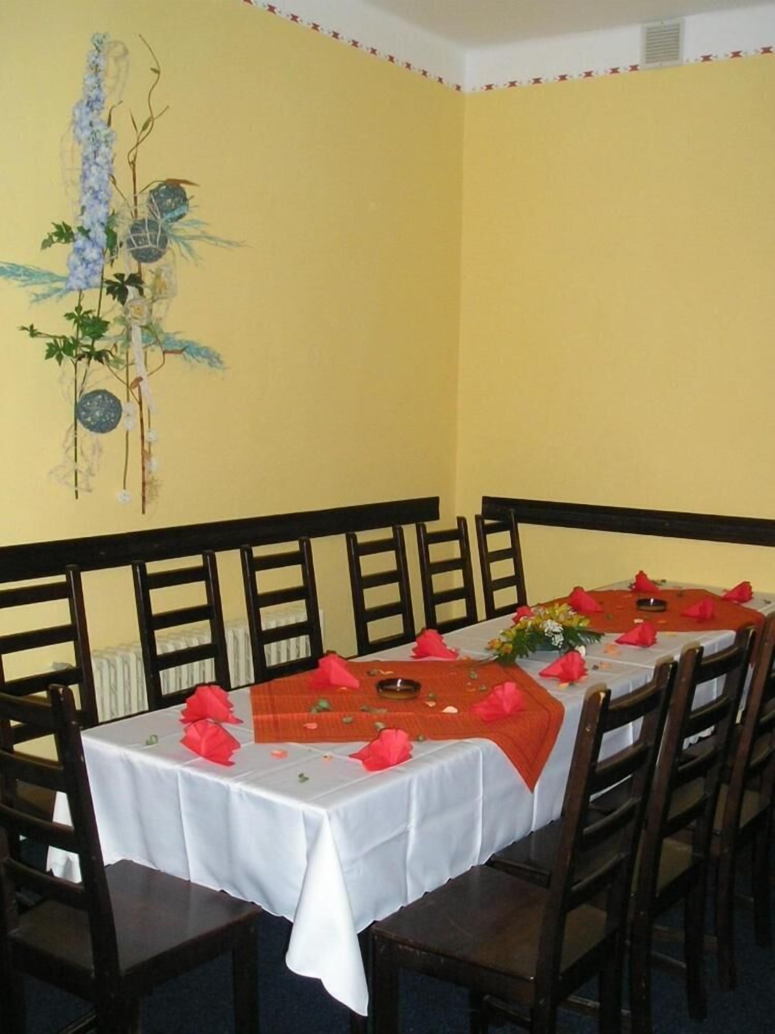 A dining area with a long table set for multiple guests, wooden chairs, and a decorative wall piece.