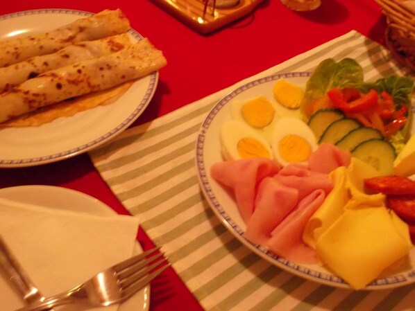 A dining table with plates of food, including a plate with sliced cucumbers, tomatoes, and cheese, and another with rolled items and eggs. - Hotel U Beránků (Libochovice)