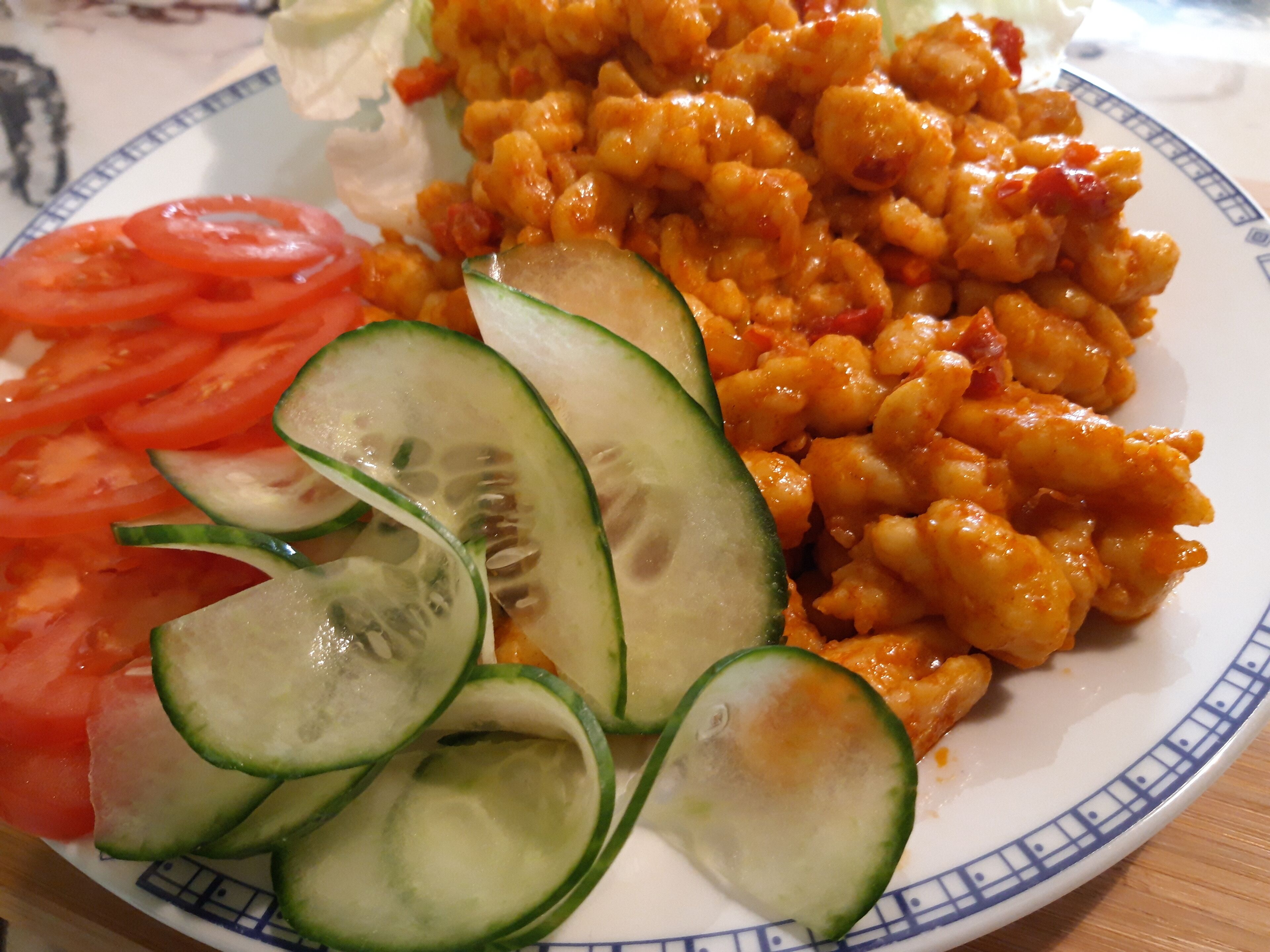 A plate with food including sliced cucumbers, tomatoes, and a dish with a red sauce.