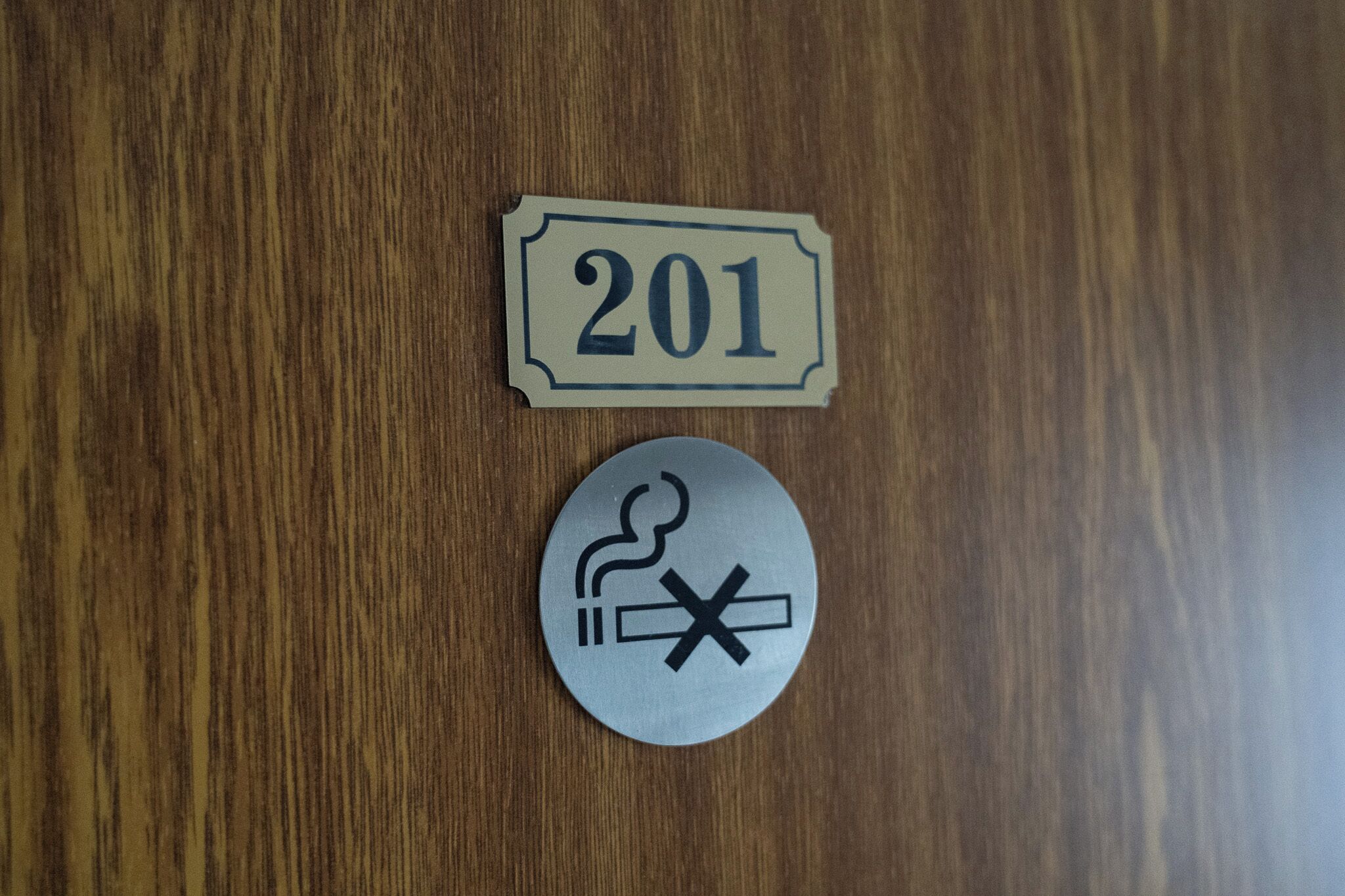 A wooden surface with a sign labeled '201' and a circular sign with a smoking symbol and a crossed-out cigarette.