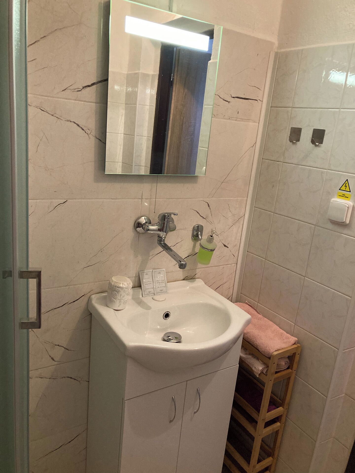 Un bagno con un lavandino bianco, uno specchio e uno sgabello di legno.