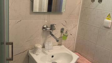 Un bagno con un lavandino bianco, uno specchio e uno sgabello di legno.