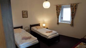 Una habitación con dos camas individuales, una ventana con cortinas florales, una lámpara colgante y un pequeño cuadro en la pared.