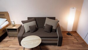 A modern living room with a sofa, a small round table, a bedside table with a lamp, and a bed. - Hotel U Beránků (Libochovice)