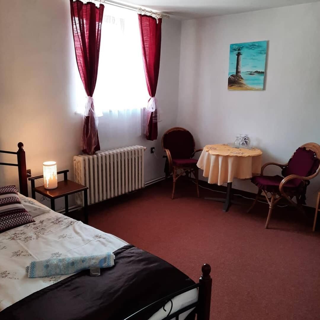 A bedroom with a bed, two chairs, a small table, a radiator, and a painting on the wall.
