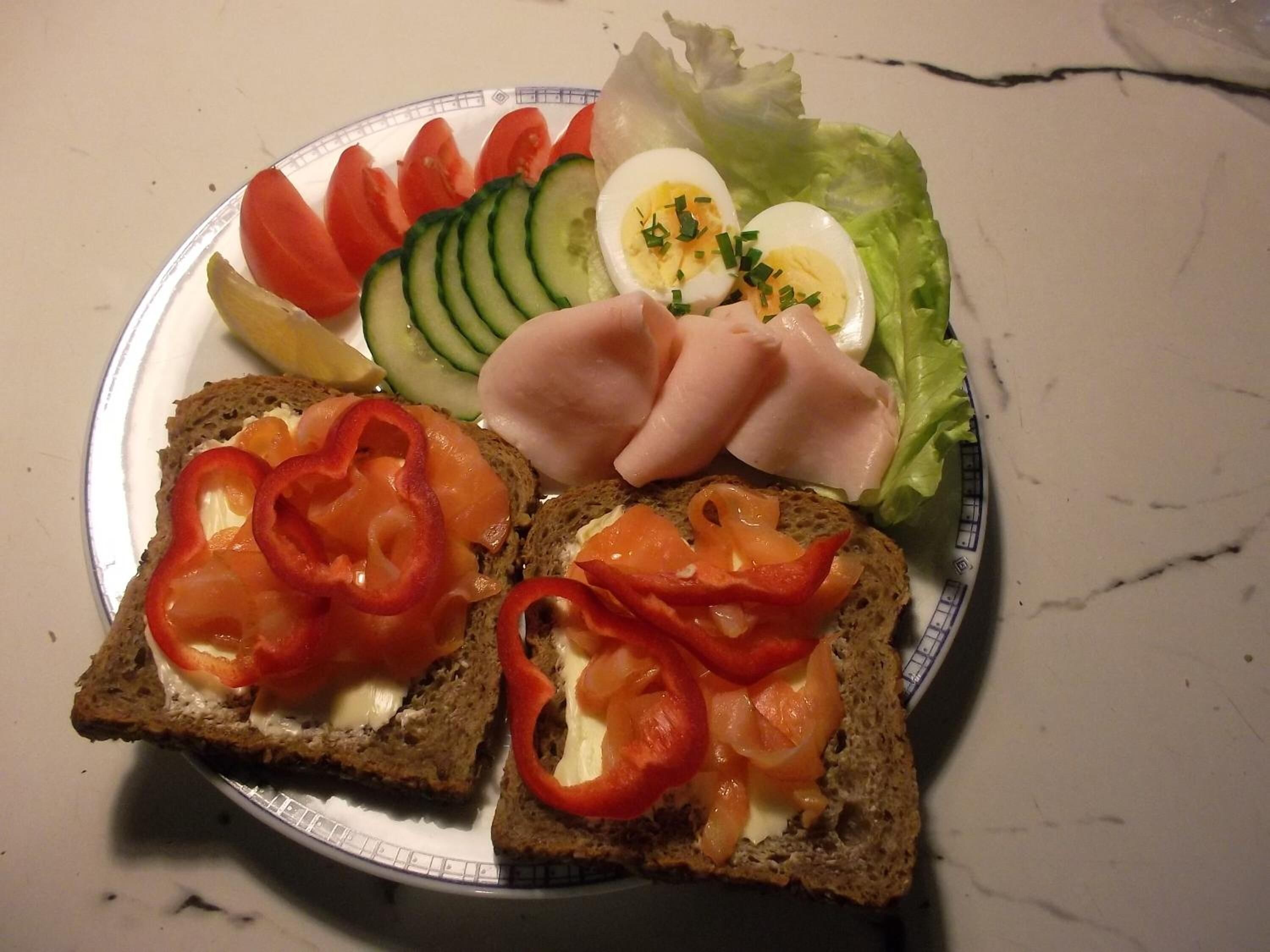 En tallerken med forskelligt mad, blandt andet brød, tomater, agurker, skinke, æg og salat.
