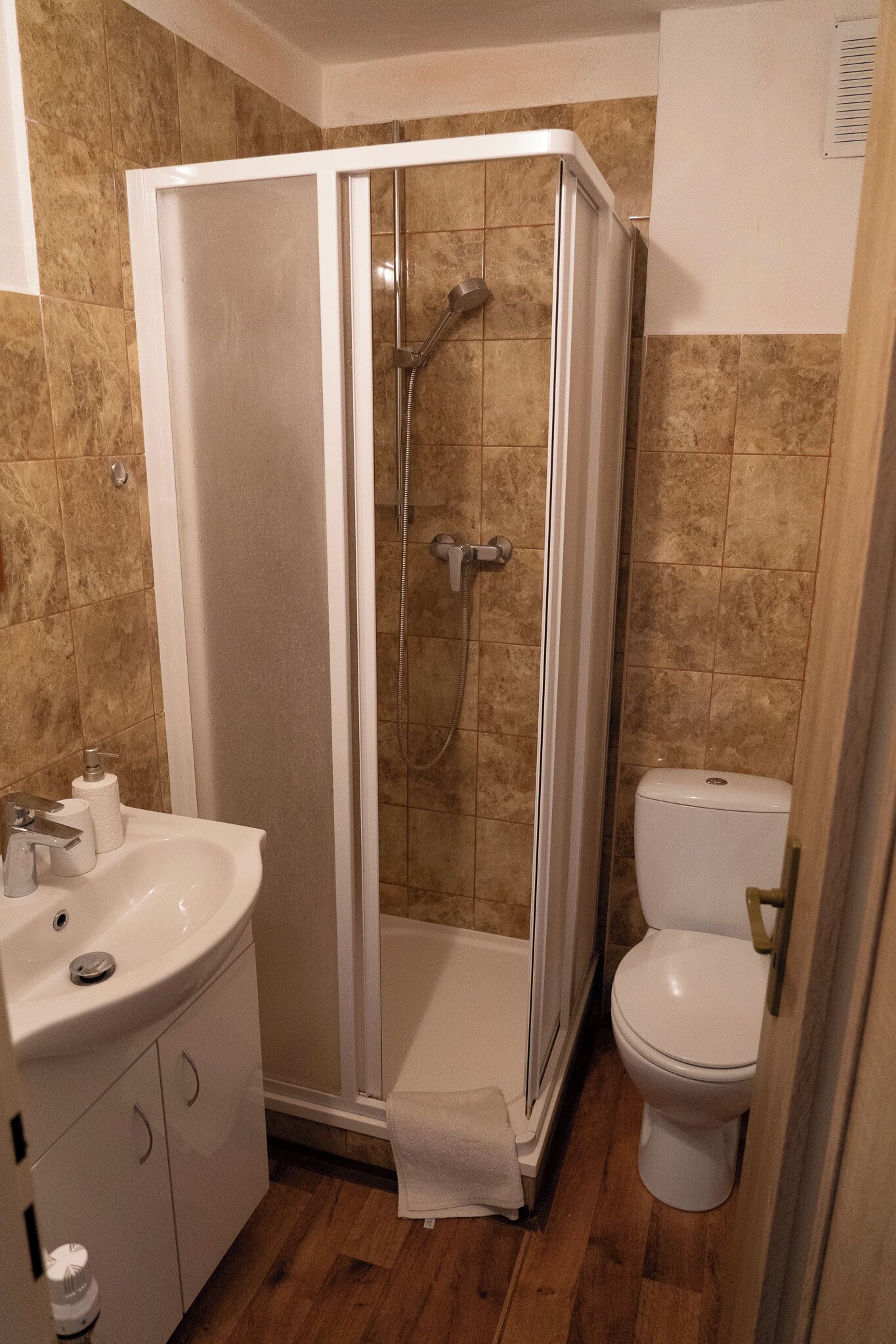 Un baño con ducha envuelta en vidrio, inodoro y lavabo con armarios.