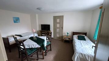 Habitación de hotel con dos camas individuales, una mesita con una silla, televisión, mesita de noche y una puerta.