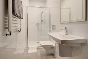 Un baño moderno con ducha de vidrio, un lavabo blanco y un inodoro.