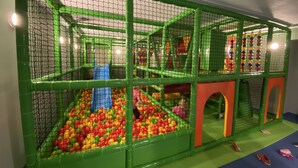 A multi-level indoor play area with netted walls, a ball pit, slides, and various play structures.