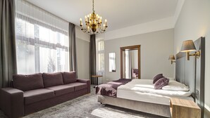 A bedroom with a bed, a sofa, a chandelier, and a small wooden table.