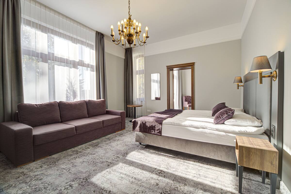 Ein Schlafzimmer mit Bett, einer Couch, einer Chandelüster und einem kleinen Holztisch.