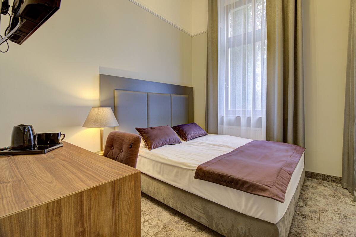Ein Hotelzimmer mit Bett, Schreibtisch, Stuhl, Lampe und einem Fenster mit Vorhängen.