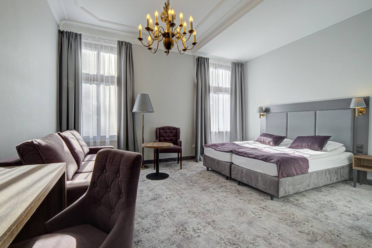 Ein Hotelzimmer mit Bett, Sofa, Sessel, Tisch und einer Deckenleuchte.
