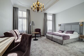 Una habitación de hotel con cama, sofá, sillón, mesa y araña.