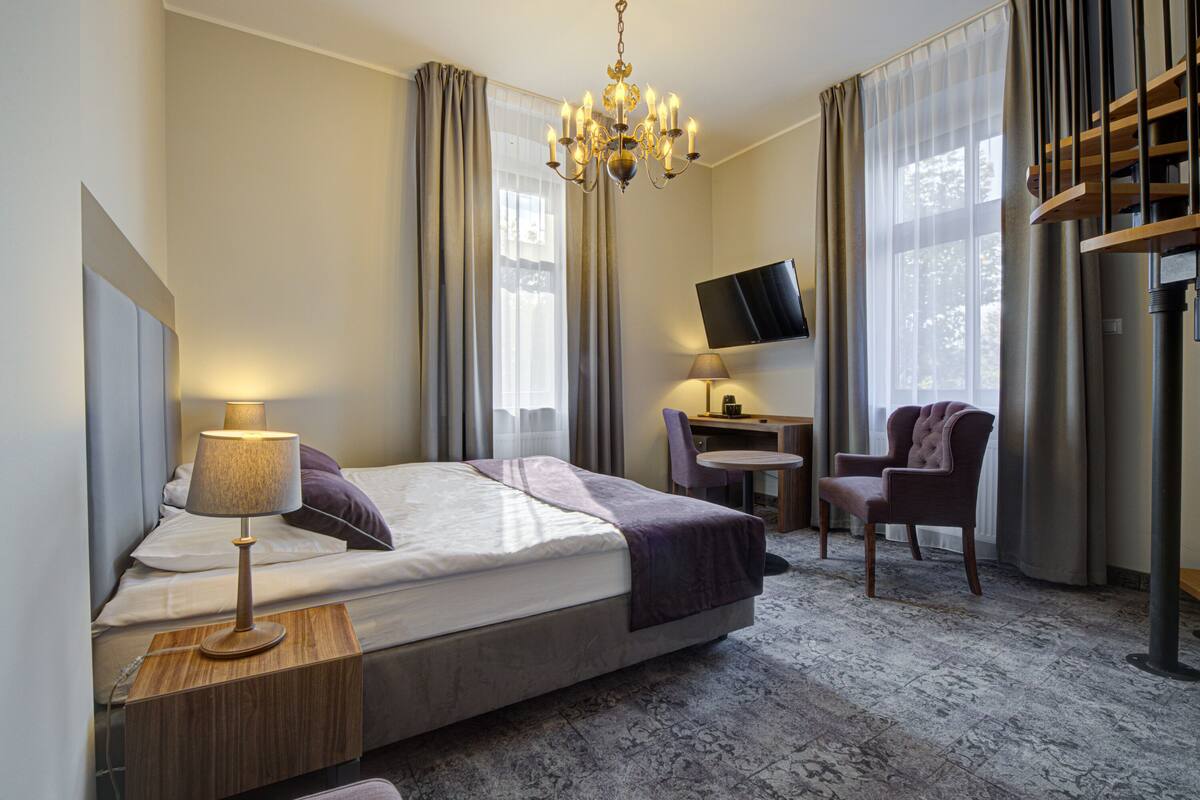 Ein Hotelzimmer mit Bett, Schreibtisch, Stuhl, Fernseher und einer Chandelier.