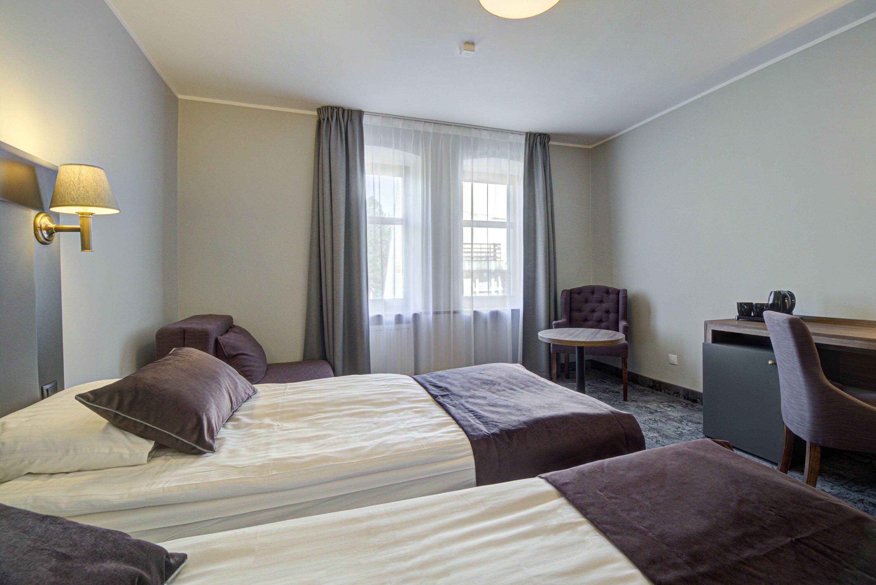 Ett hotellrum med två sängar, ett skrivbord, en stol och en lampa.