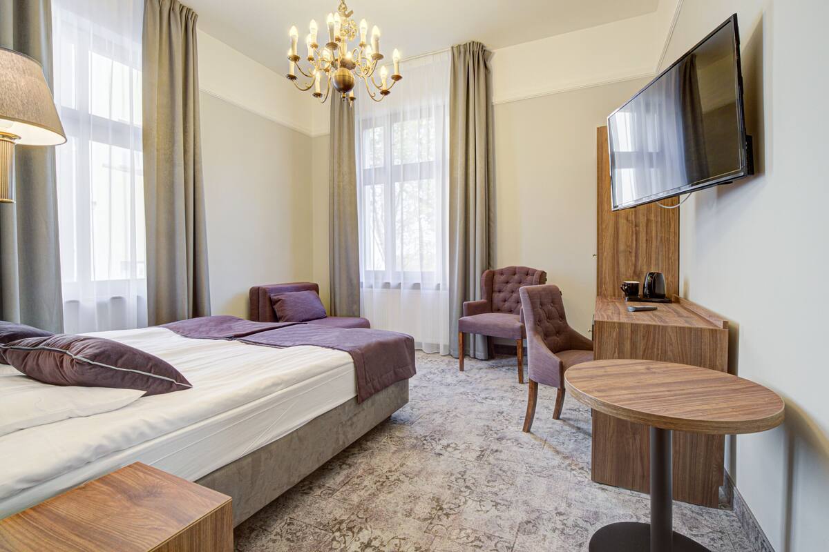 Ein Hotelzimmer mit einem Bett, zwei Stühlen, einem kleinen Tisch, einem Fernseher und einer Deckenleuchte.