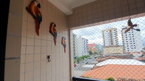 A room with tiled walls, a balcony with a view of urban buildings, and decorative parrot figures.