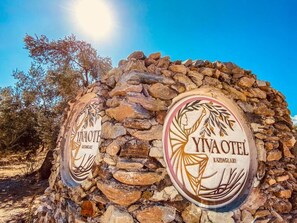 A stone wall with two circular signs for "Ivaote" and "Yivaotel" hotels, indicating their names and location in Kazdaglari. - Yiva Kazdaglari (Edremit)