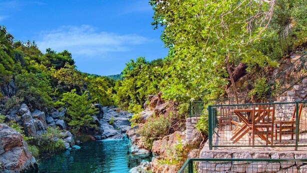 A clear view of a river with rocky banks, surrounded by lush greenery. There is a wooden deck with a chair and a fence. - Yiva Kazdaglari (Edremit)