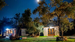 A nighttime scene of a small, two-story building with a visible balcony and a lit interior, surrounded by trees and a clear sky. - Yiva Kazdaglari (Edremit)