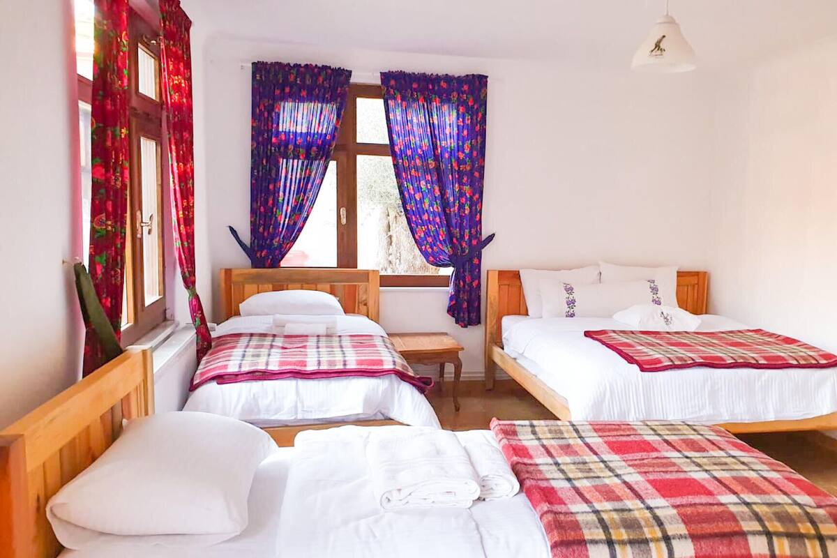 A room with two beds, a wooden headboard, a small table, and a window with curtains.