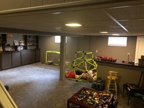 A room with a play area including a green climbing structure, a small playhouse, and a table with various toys.