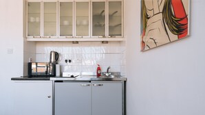 Una cocina compacta con armarios blancos, un hervidor de acero inoxidable y un lavamanos.