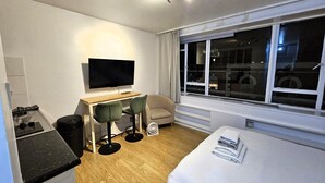 Una habitación de hotel moderna con una cama, un escritorio con silla, un televisor y un amplio ventanal.