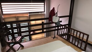 Ein Zimmer mit einem Etagenbett, einem kleinen Tisch, einem Hängesessel und einem Fenster mit Jalousien.