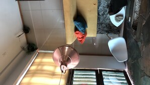 Ein Zimmer mit einer Couch, einer Pendelleuchte, einer Steinwand und einem Fenster mit Jalousien.