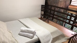 Ein Einzelbett mit weißer Bettwäsche und einem gefalteten Handtuch, ein Holz-Kopfteil und eine Steinsäule im Hintergrund.