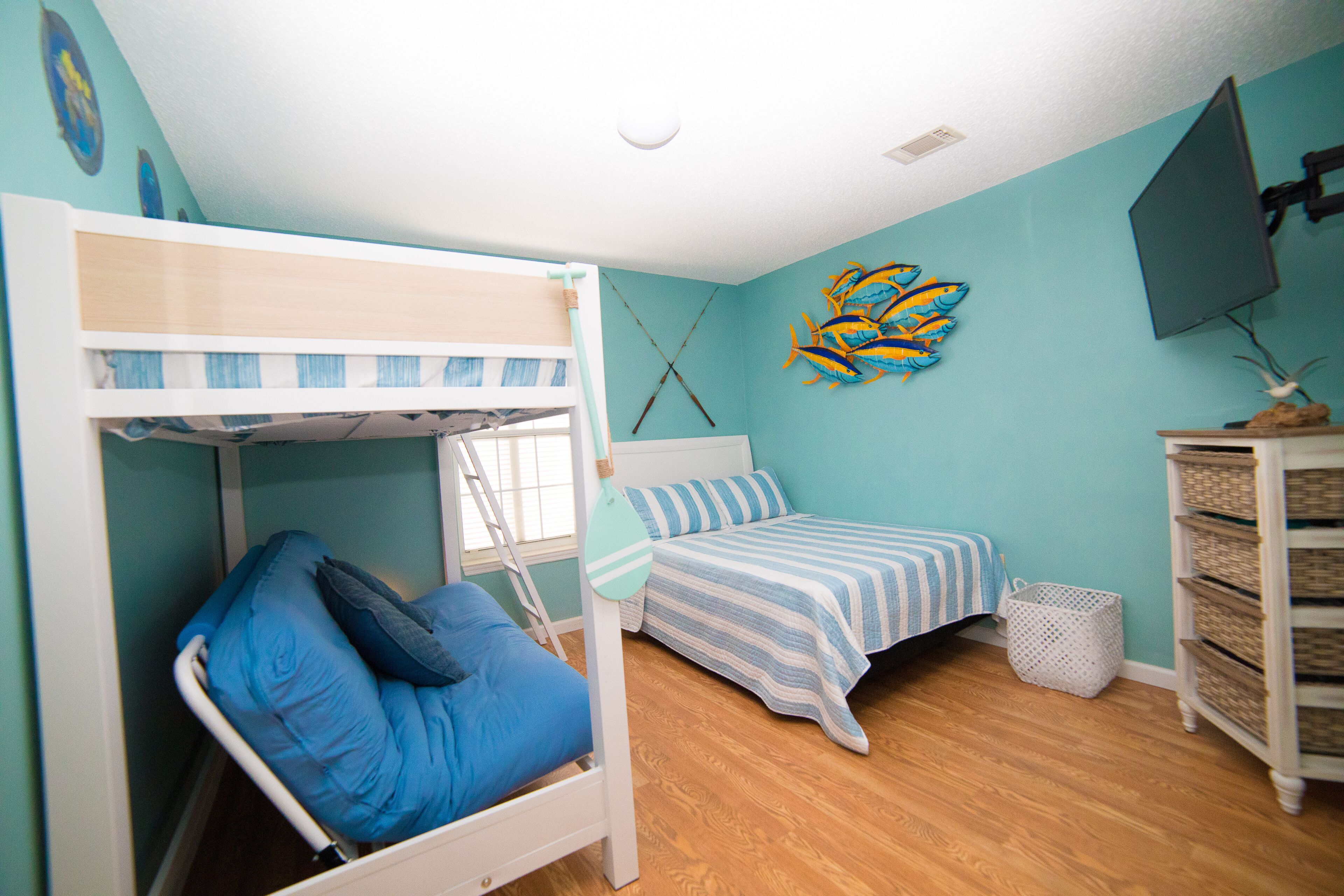 A bunk bed room with a window, a bed with striped bedding, a wall decoration, and a TV mounted on the wall.