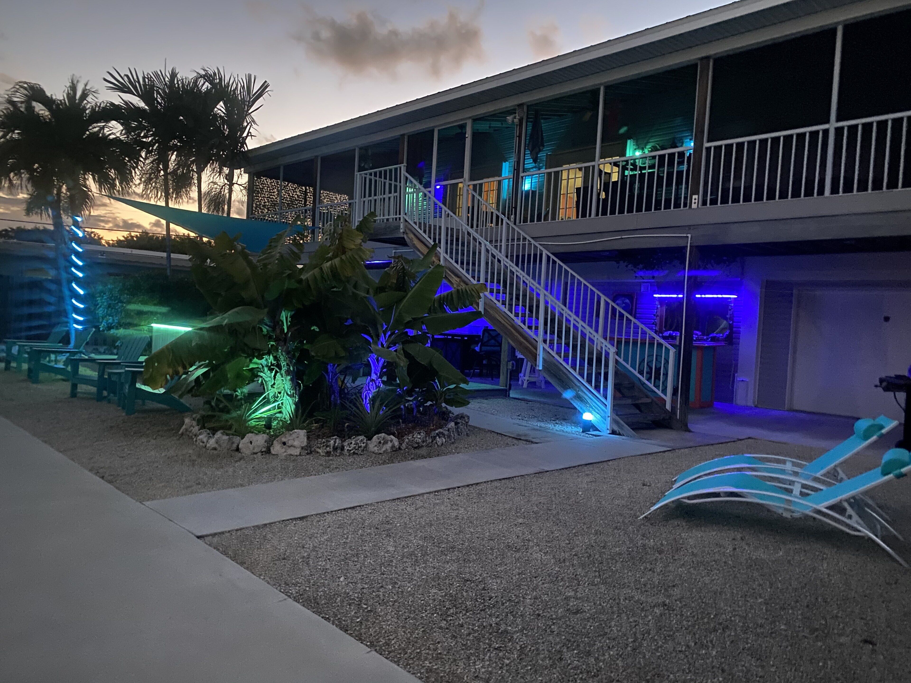 A hotel with a covered outdoor seating area, a staircase, and a pool.